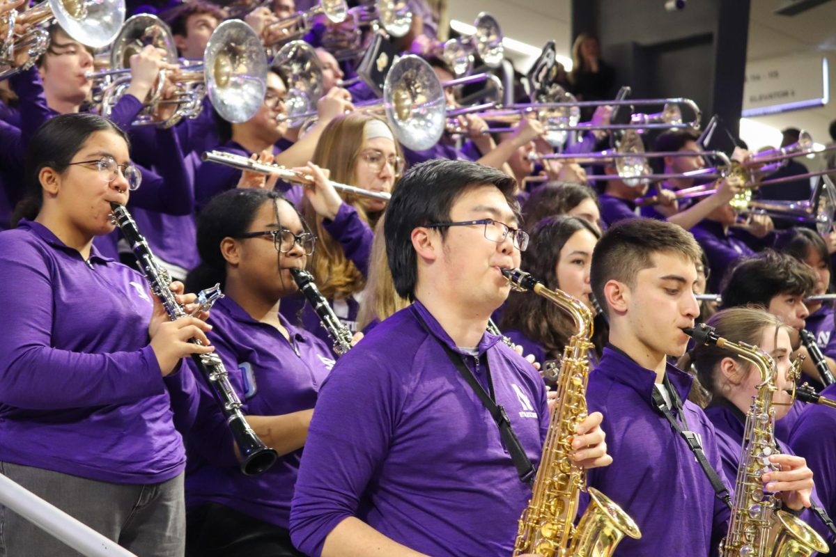 The Northwestern University ‘Wildcat’ Basketball Band wearing purple quarter-zip jackets plays in the stands.