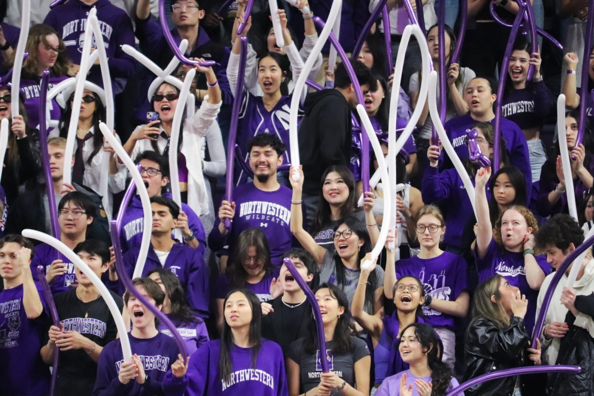 Students in the stands cheer as they hold purple and white balloons.