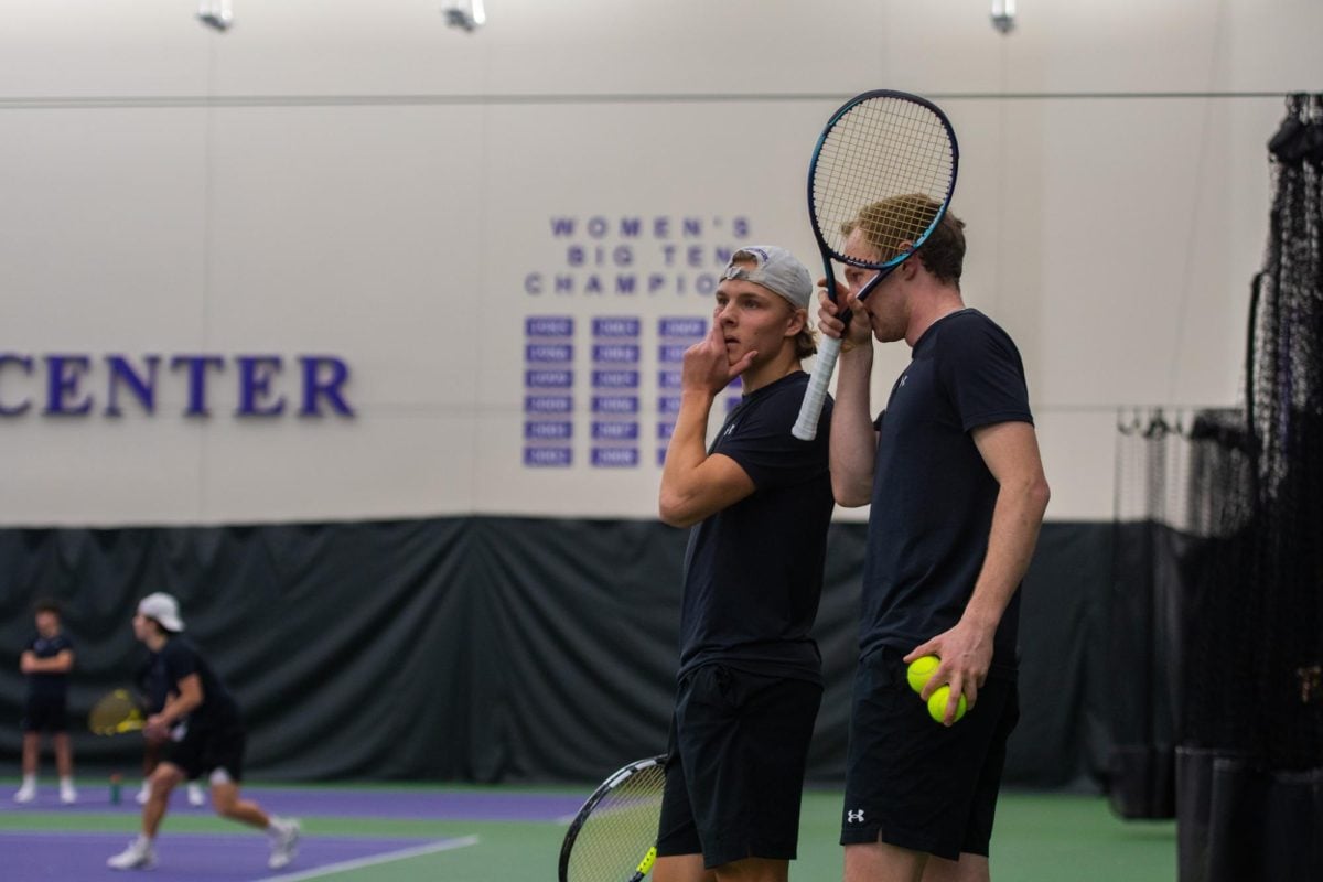 Northwestern tennis doubles partners Gleb Blekher and Felix Nordby talk to each other while holding tennis balls and rackets.