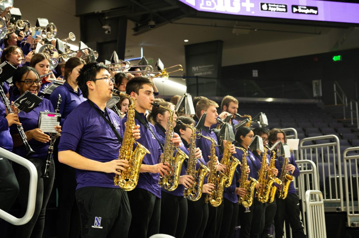 Northwestern University Basketball Band members, wearing purple quarter-zip jackets, play a song in the stands during a timeout.