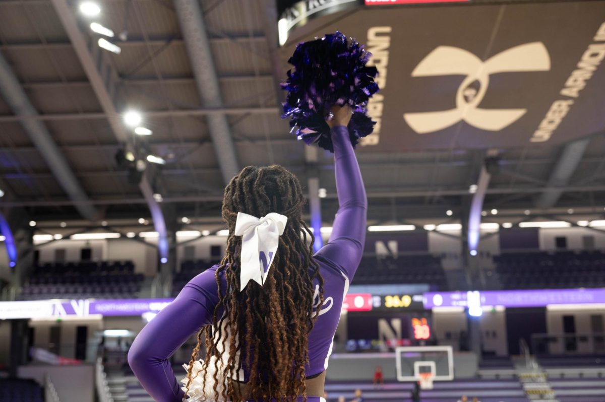 An NU cheerleader in a purple uniform raises a purple pom pom into the air.
