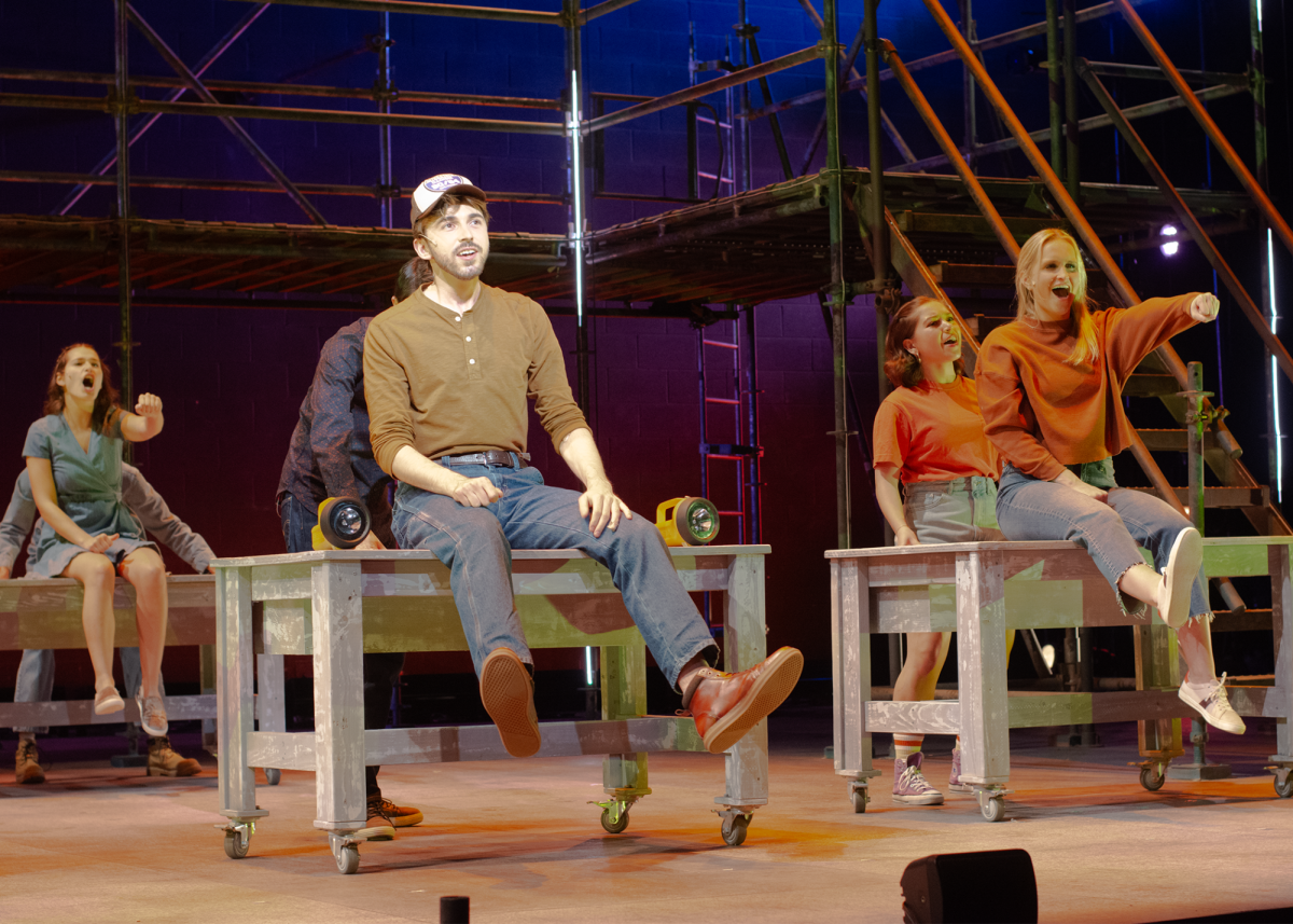 Cast members of “Working” sit on top of benches and pantomime driving cars onstage.