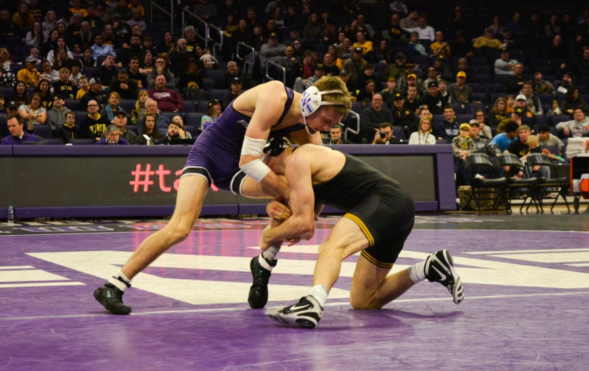 133-pounder Patrick Adams, wearing a purple singlet, defends against a takedown attempt from his opponent, wearing black, who has control of his left leg.