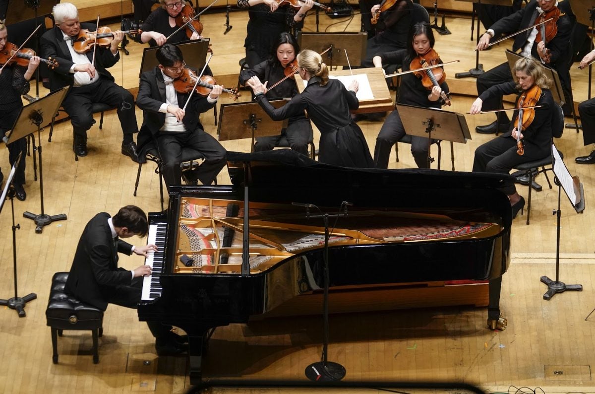 A pianist playing the piano in front of an orchestra and a conductor.