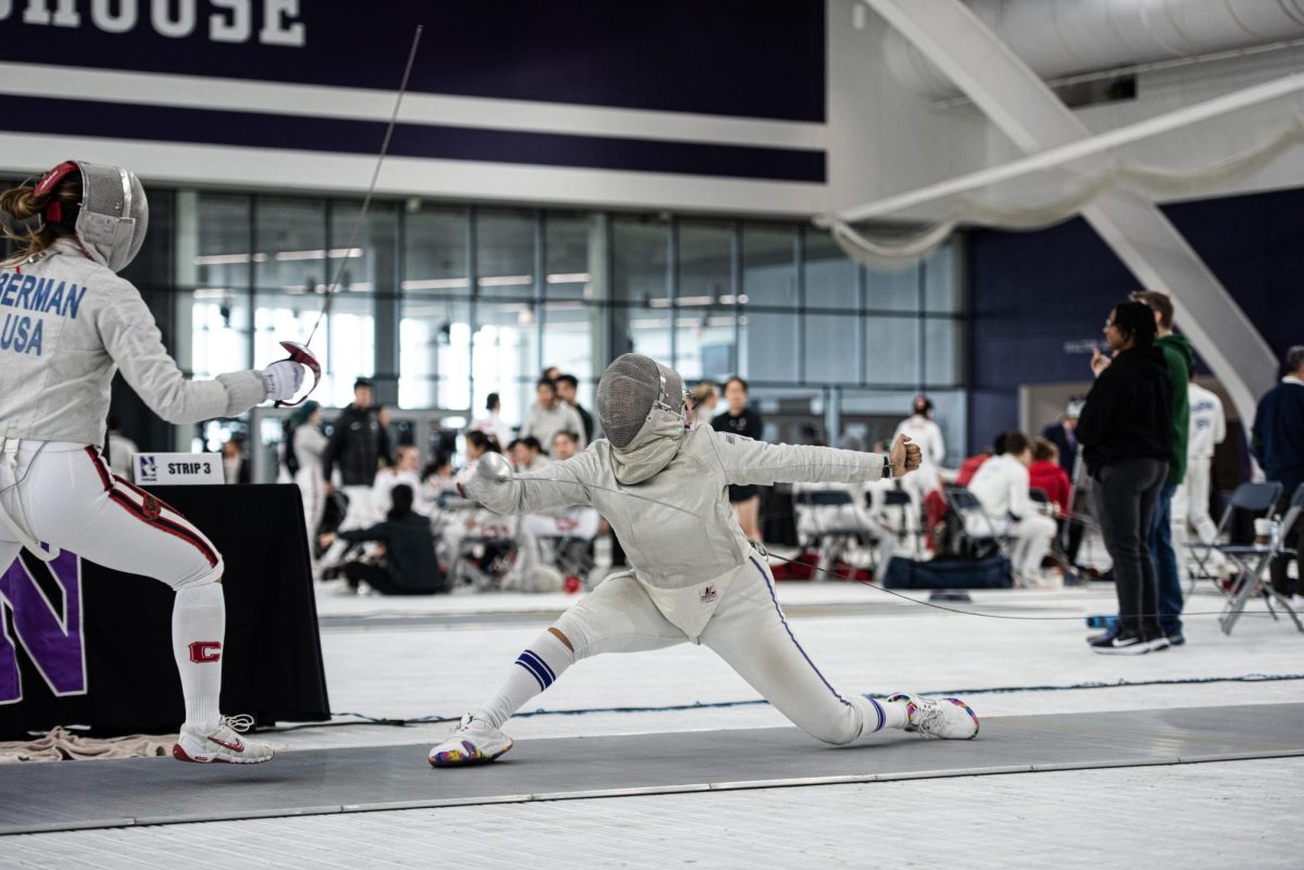 A Northwestern fencer wearing white and purple and holding a saber lunges at a Cornell Fencer wearing white and red.