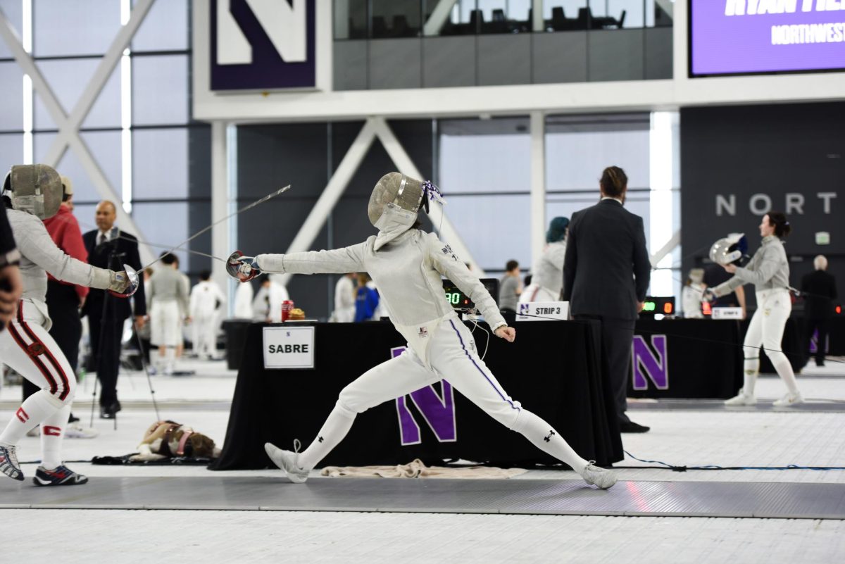 A Northwestern fencer wearing white and a mask holds a saber and lunges forward.