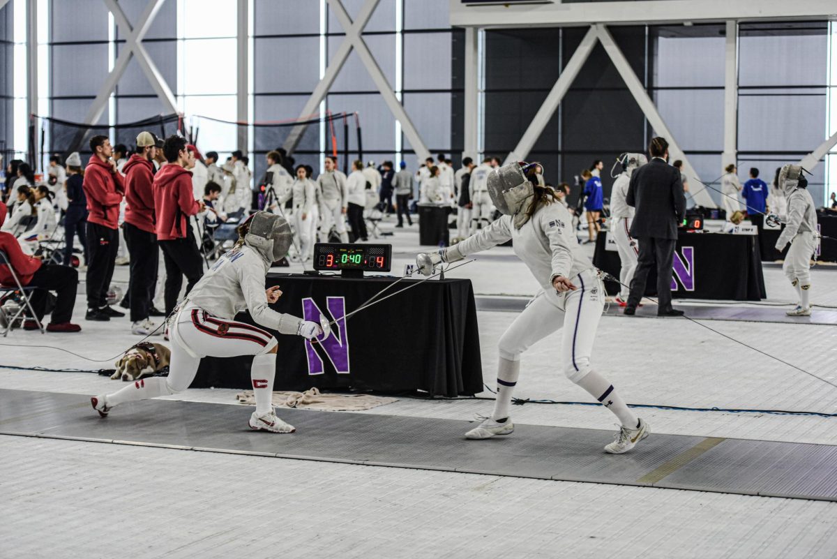 A Northwestern fencer in a white and purple uniform points a saber at an athlete wearing white and red, who is lunging with their saber.