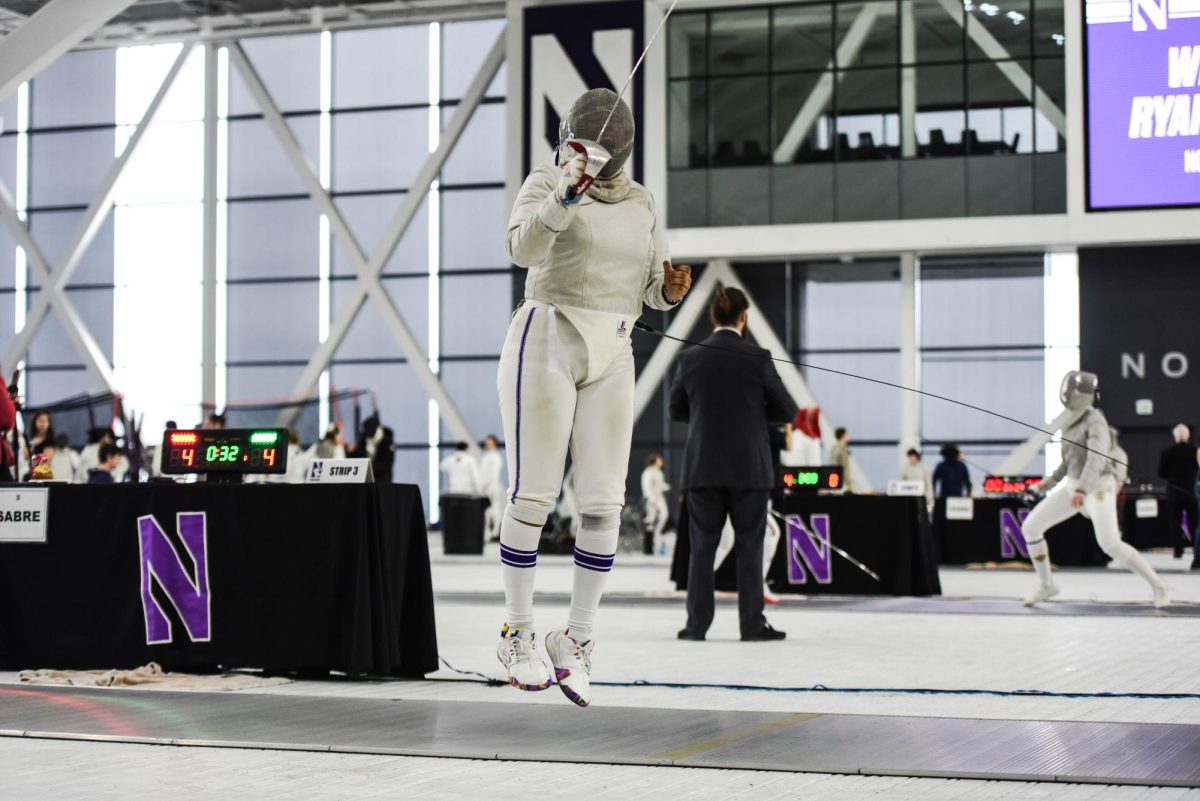 A Northwestern fencer wearing white and purple jumps upward while holding a saber.