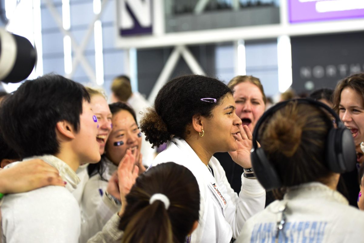 A Northwestern fencer in white yells while surrounded by other athletes who are also yelling.