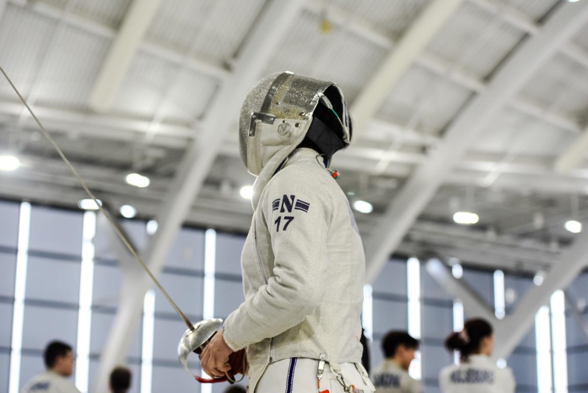 A Northwestern fencer in white and a gray mask holds a saber.