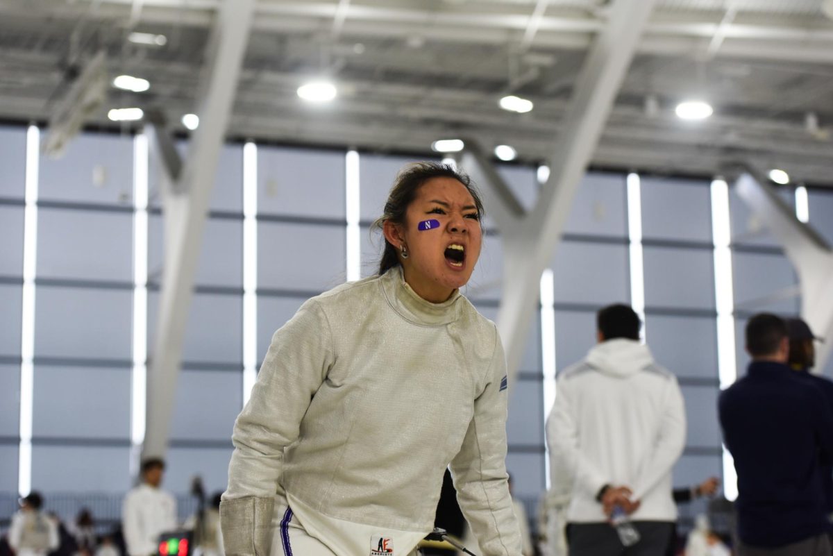 A Northwestern fencer wearing white and purple face tape yells.