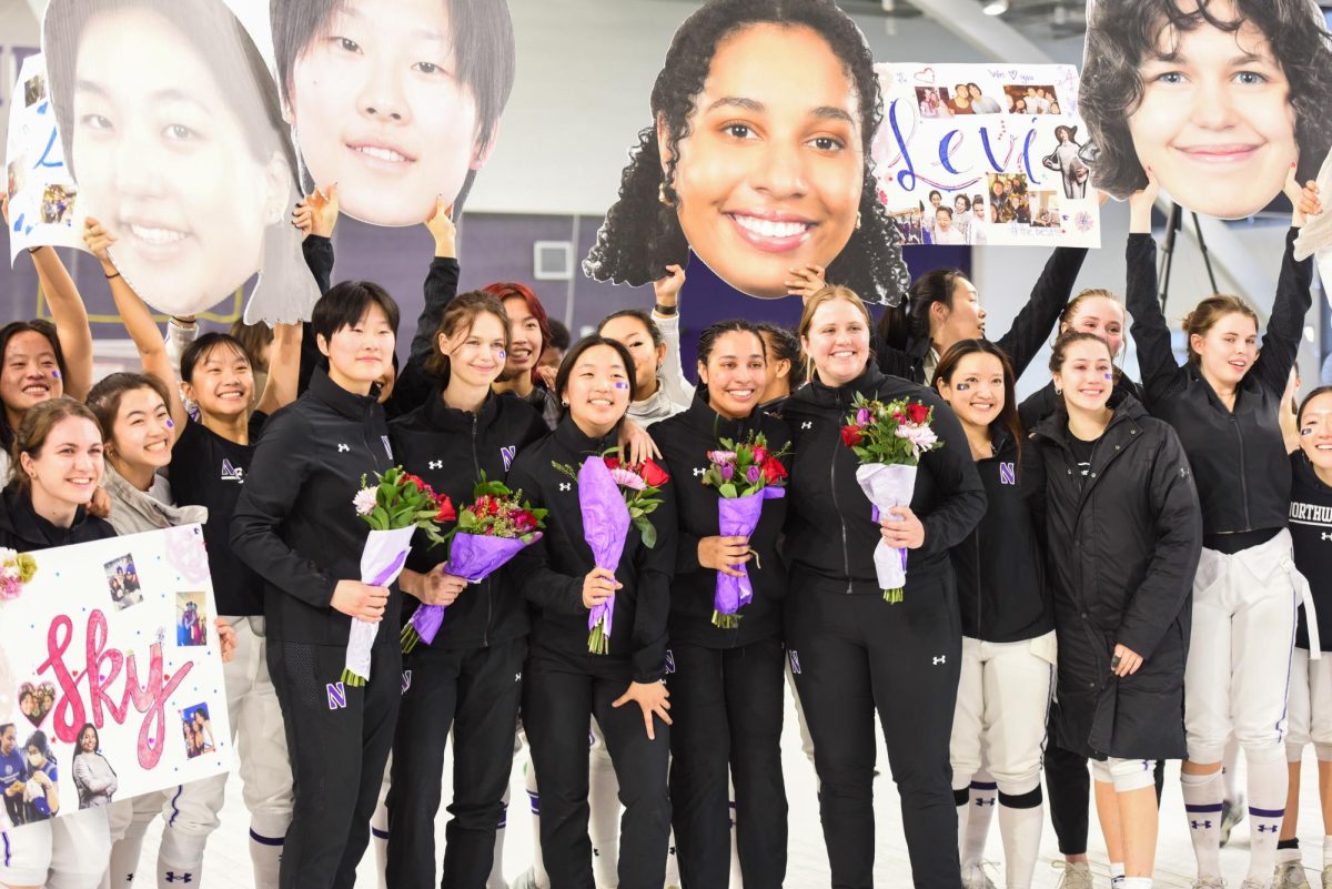 The Northwestern Women’s Fencing Team, holding flowers, are surrounded by athletes holding large pictures of faces and posters.