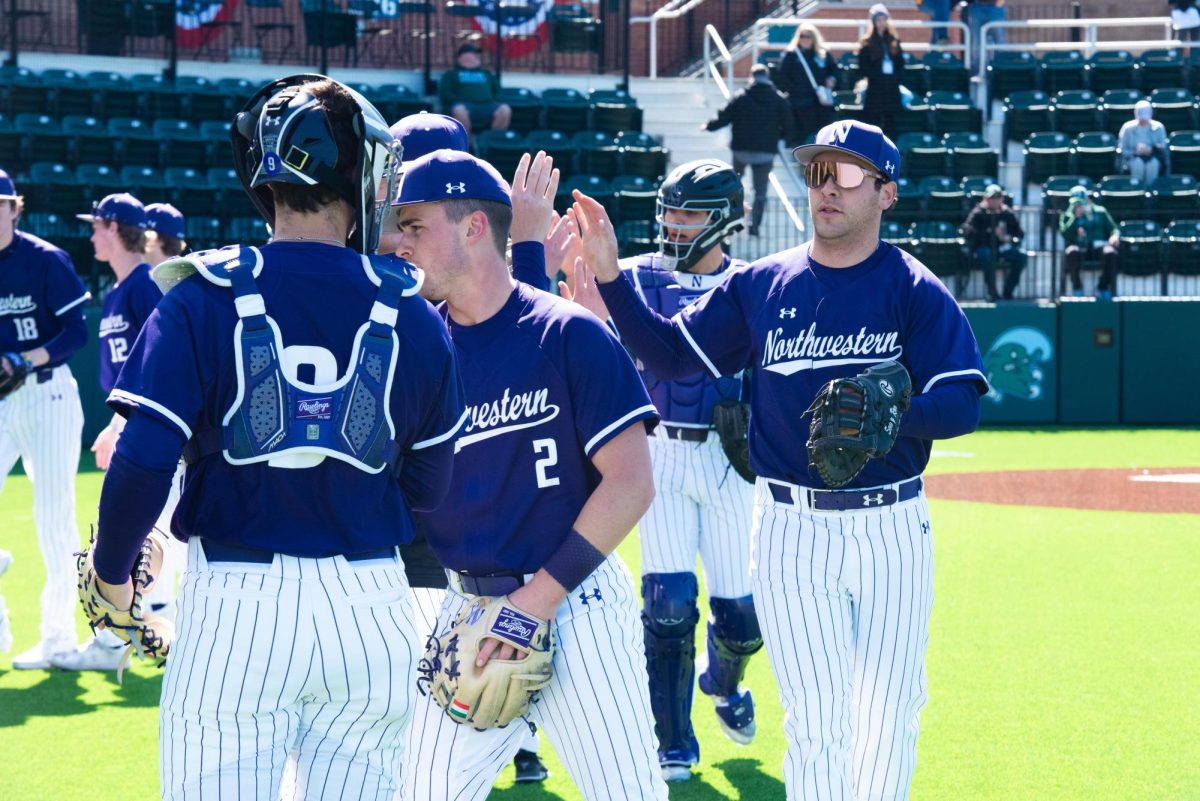 Northwestern baseball players wearing purple uniforms high five each other.