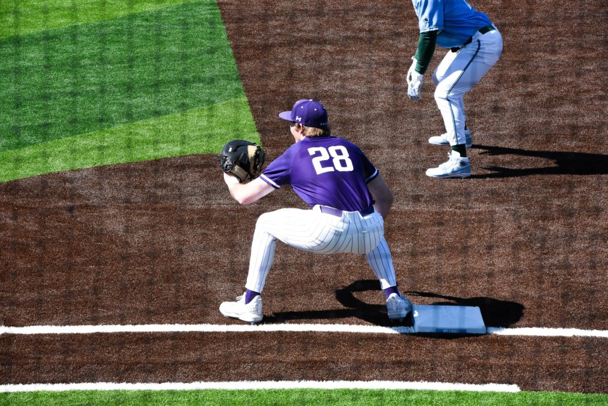A Northwestern baseball player wearing a purple number 28 jersey crouches and extends their baseball glove.