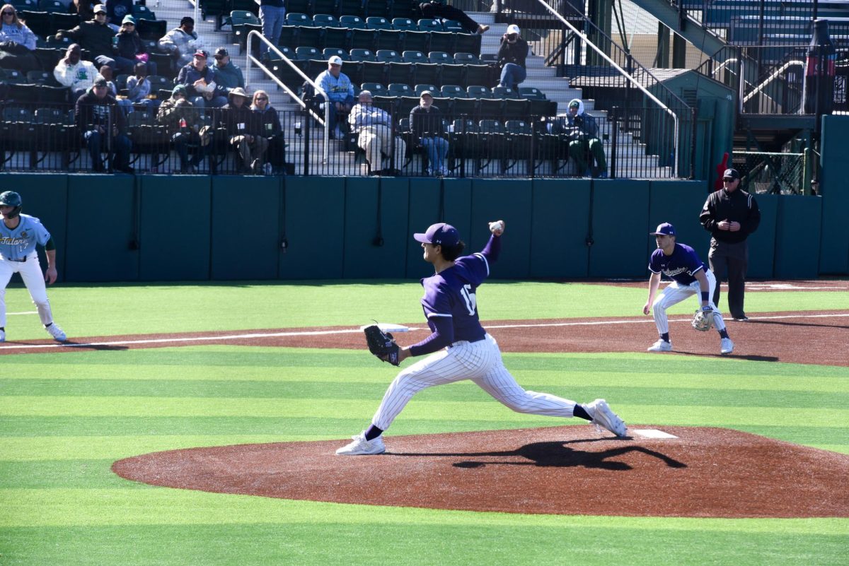 A Northwestern baseball player wearing purple pitches a baseball as people watch in the stands.