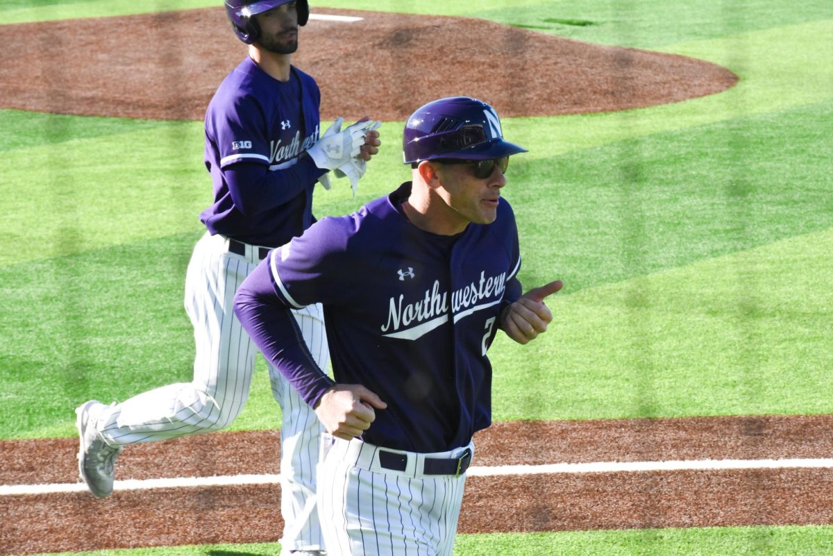 A Northwestern baseball coach wearing purple and sunglasses runs.