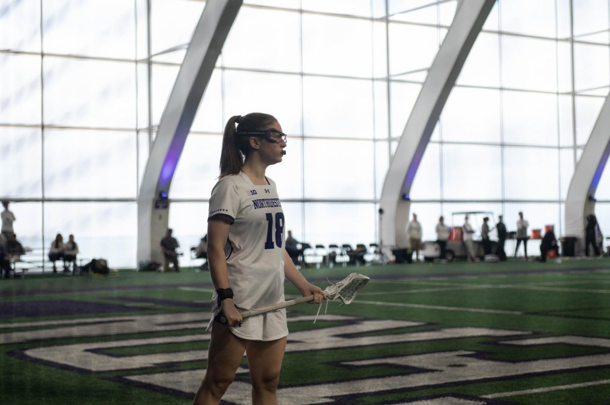 Holmes stands holding her lacrosse stick in between plays.