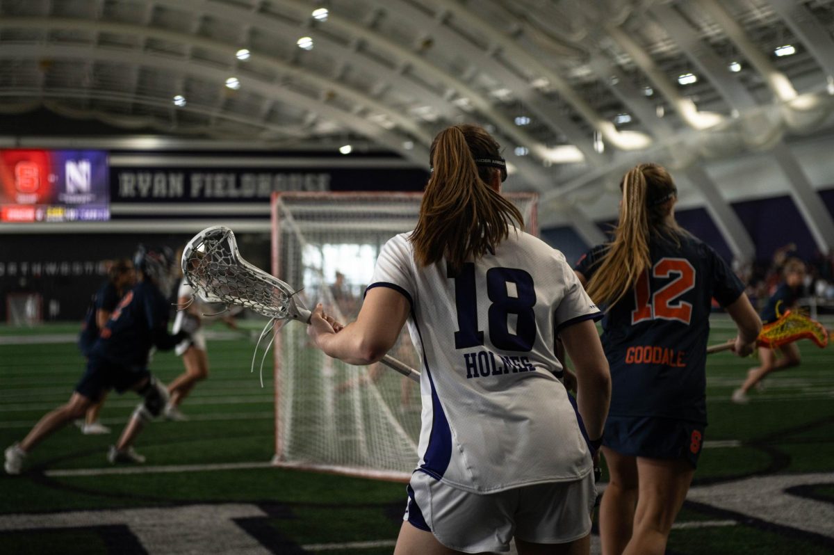 Senior attacker Leah Holmes runs out from behind the net, holding a lacrosse stick.