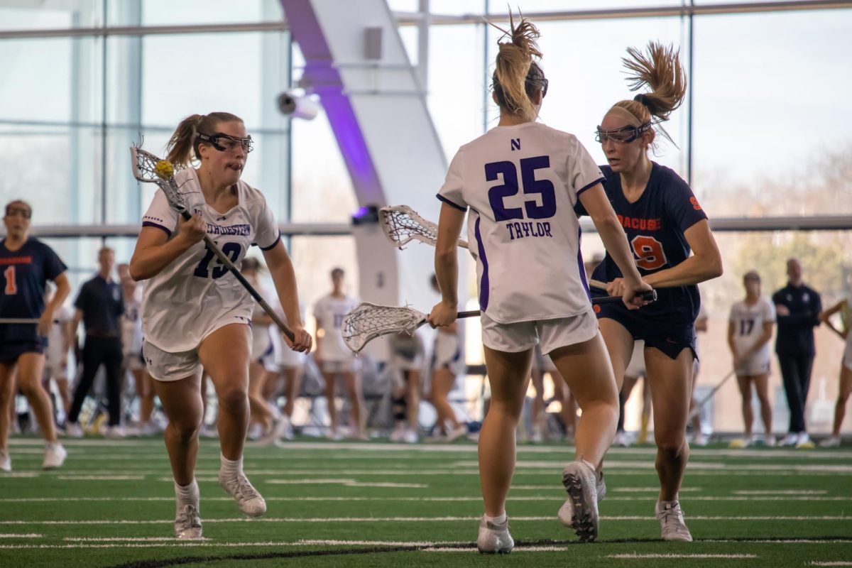 Junior midfielder Samantha Smith, wearing a white and purple uniform, runs forward with a lacrosse stick with the ball.