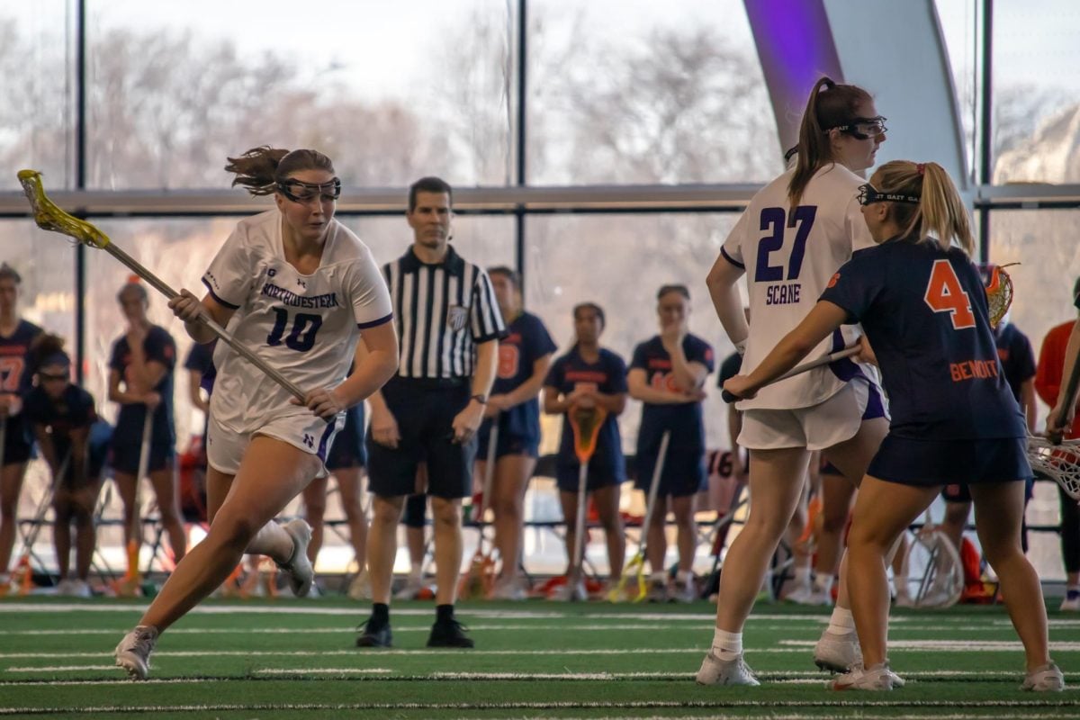 Graduate attacker Dylan Amonte runs forward with a lacrosse stick and the ball. Ahead are sixth-year attacker Izzy Scane and an opponent.
