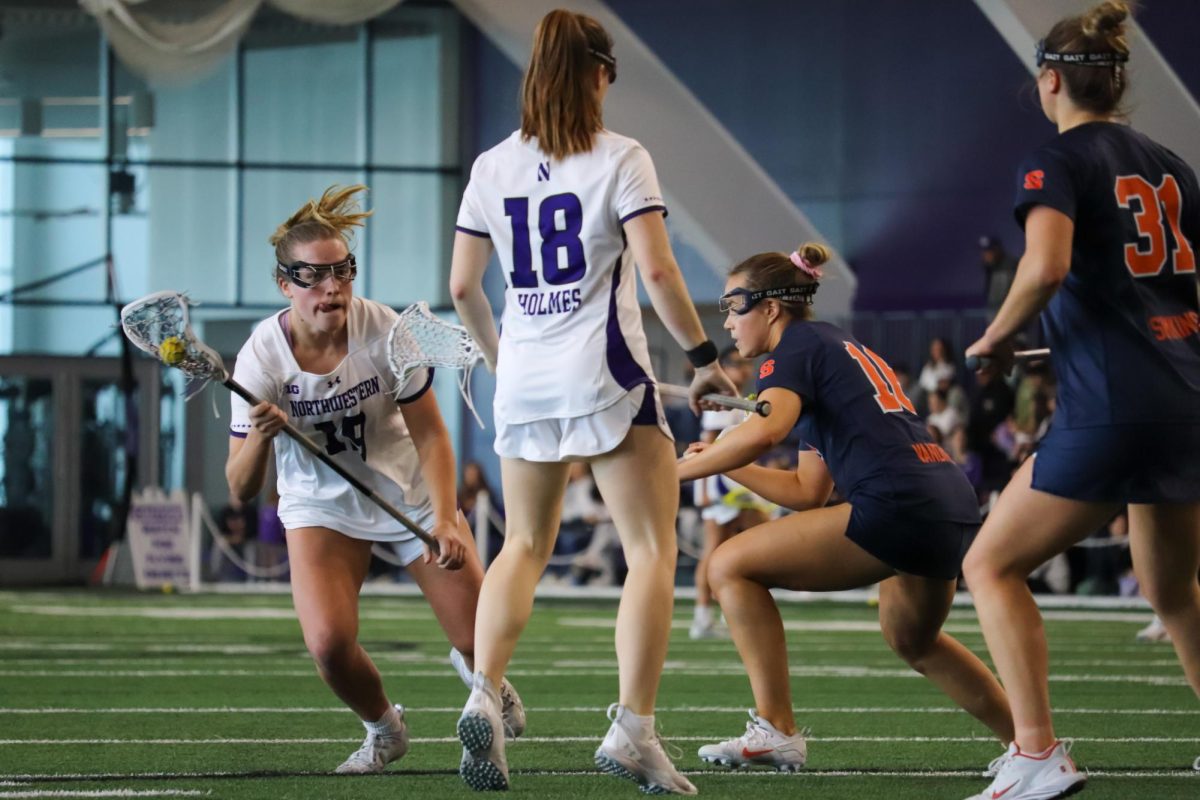 A lacrosse player in a white uniform runs toward a teammate and two opponents in blue and orange uniforms.