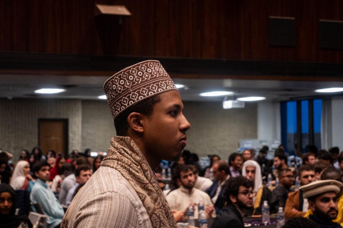 A Muslim student wearing a kufi, a traditional Islamic cap, stands in front of hundreds of attendees.