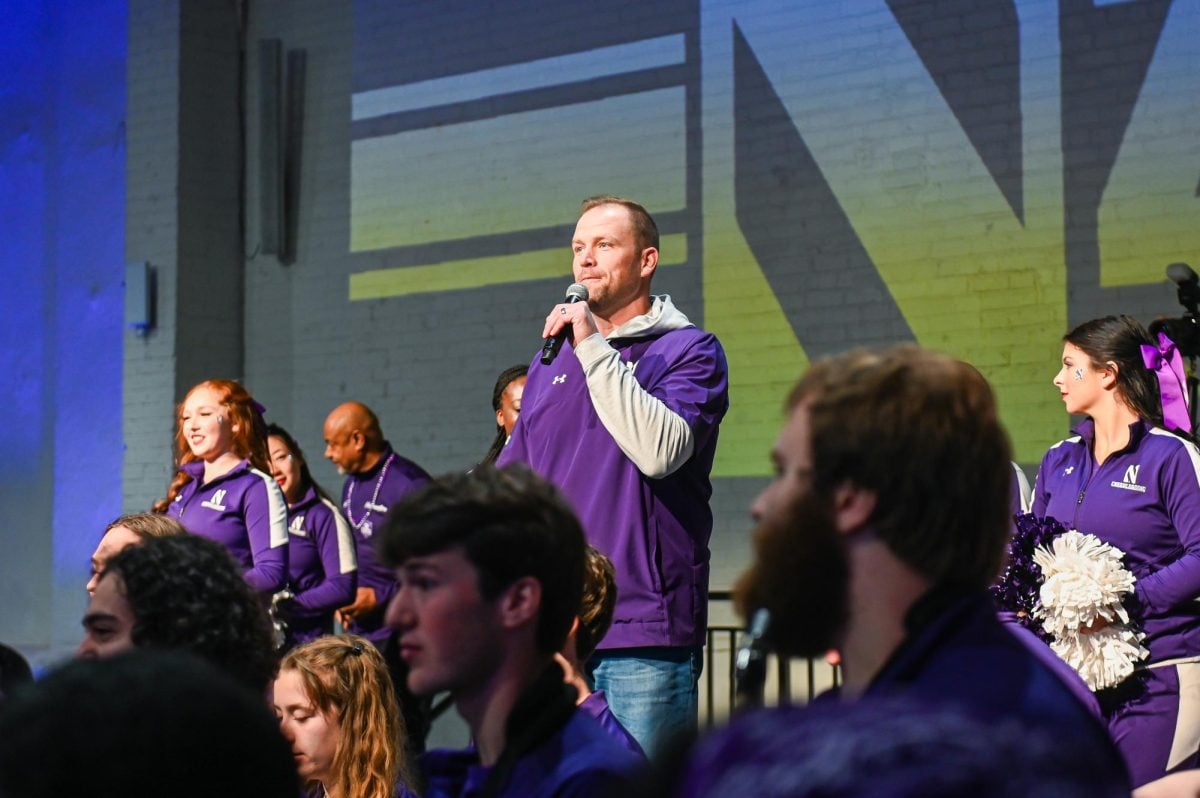 Northwestern football head coach David Braun speaks into a microphone, addressing the crowd.
