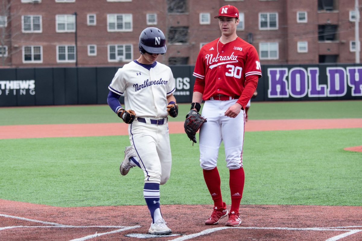 A Northwestern baseball player steps on home plate next to a player in a red uniform.