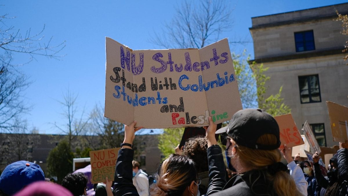 A person turned away from the camera holds up a sign that reads “NU Students Stand With Columbia Students and Palestine.”