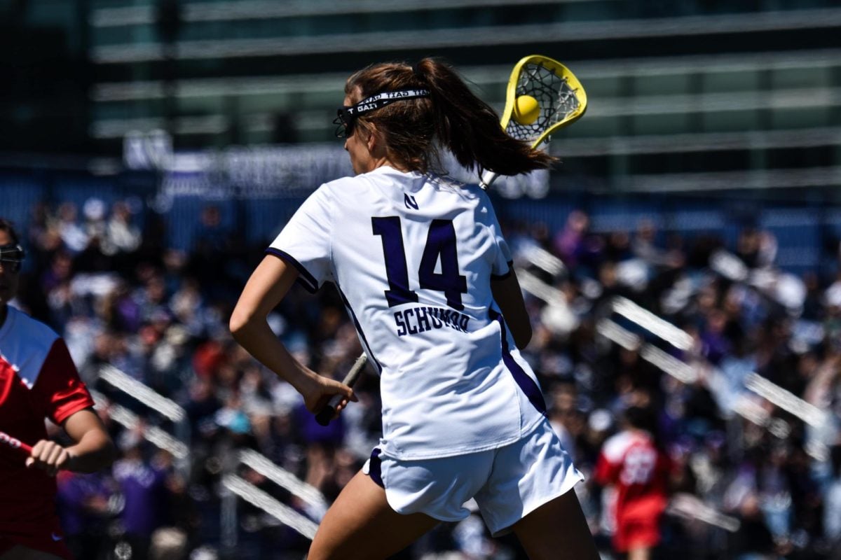A Northwestern lacrosse player wearing white runs with the lacrosse ball in her stick.