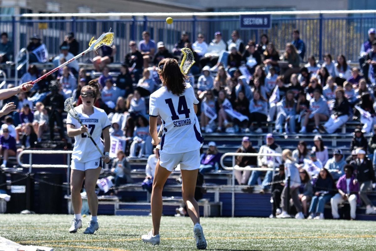 A Northwestern lacrosse player passes the ball to another Northwestern player.