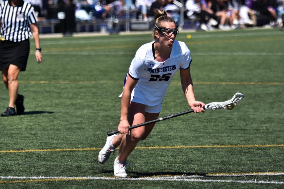 A Northwestern lacrosse player wearing white runs with the ball in her stick. 