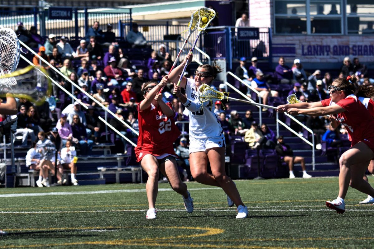 A Northwestern lacrosse player wearing white prepares to shoot a ball as players in red try to win back control.