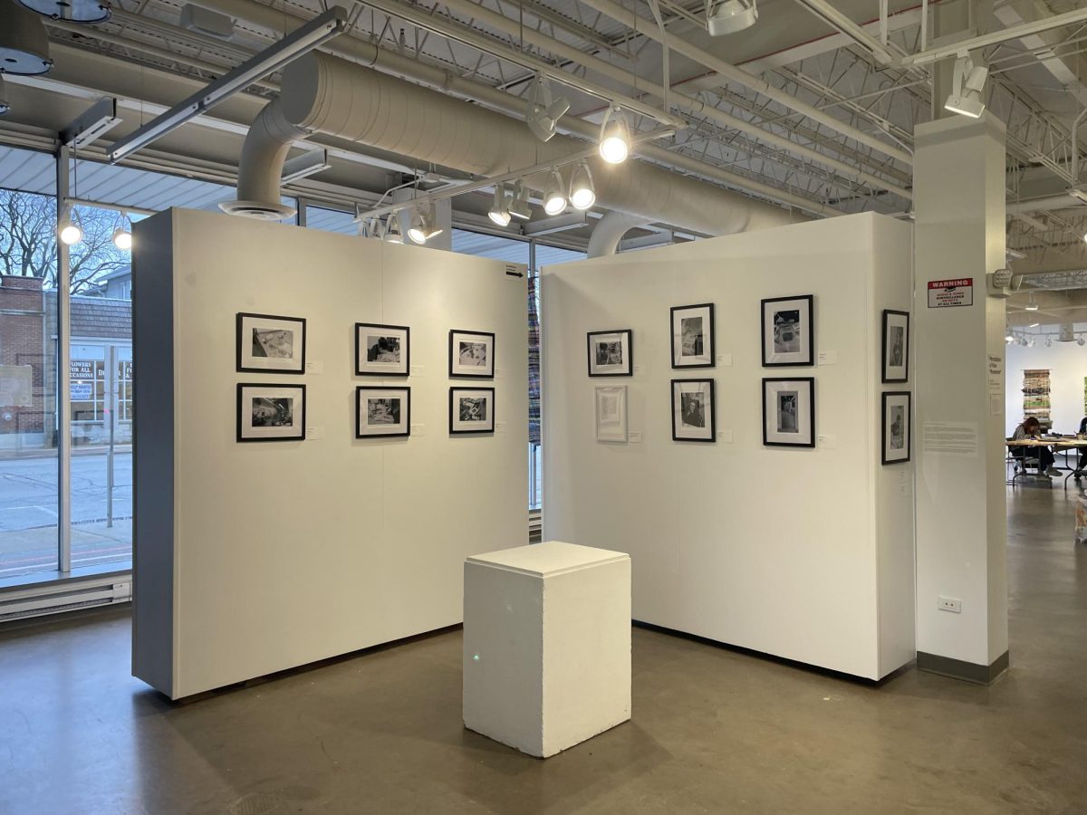 Framed black and white pictures hang on two white walls inside an art gallery.