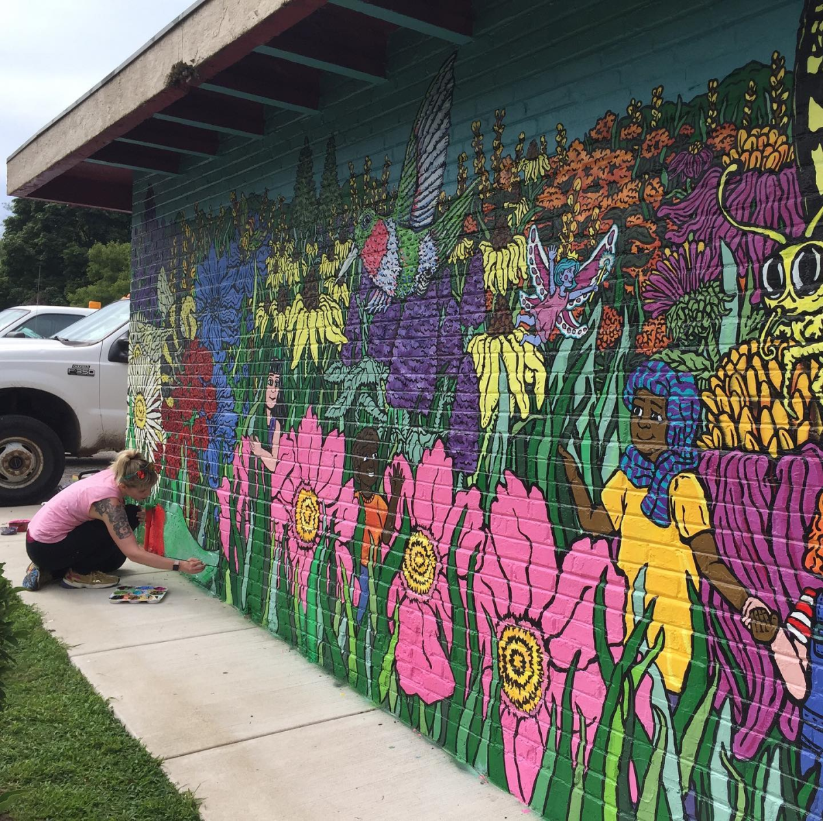 A person paints a bright, floral mural on a brick wall.