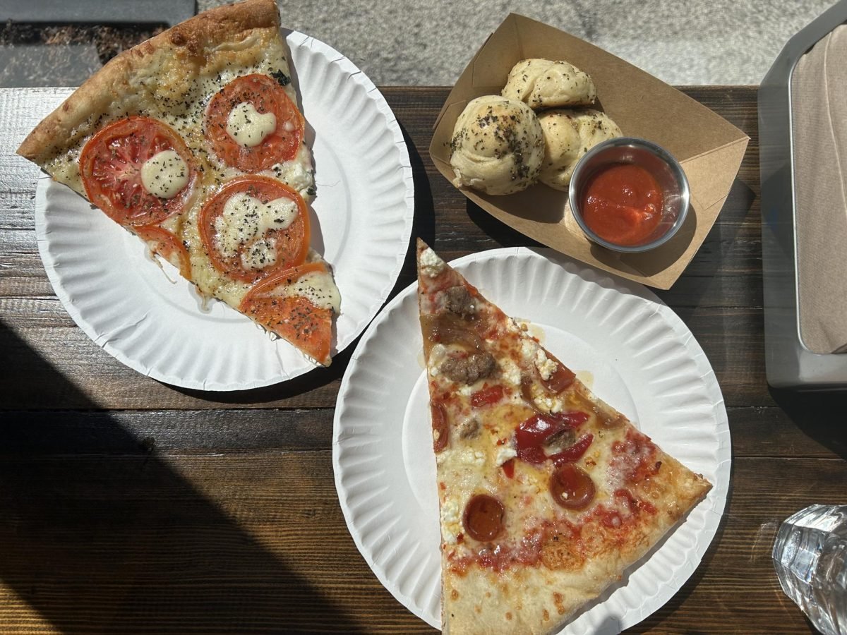 Two white plates with a Raccoon slice (topped with pepperoni, sausage, pickled peppers, caramelized onions and goat cheese) and Margherita slice and a brown tray with three garlic knots and marinara dipping sauce.