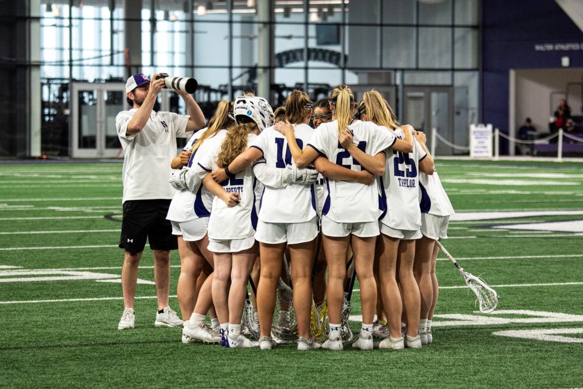 Members of the Northwestern lacrosse team huddle in the middle of the field.