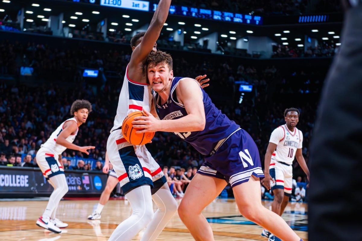A basketball player in purple with the ball runs into an opposing team player, who tries to block them.