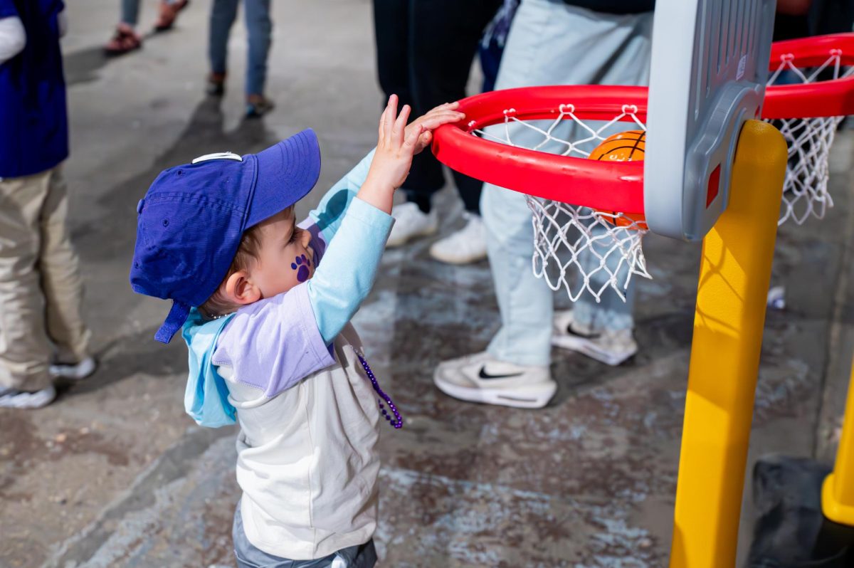 A child with a purple cap throws a plastic basketball into a small basketball hoop.