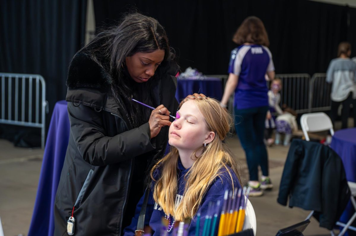 A child sits while another person face paints.
