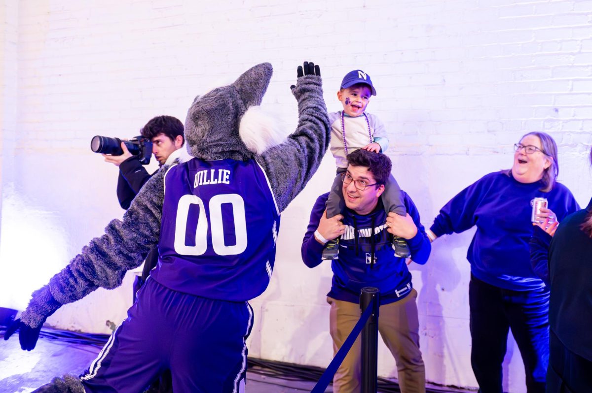 Willie the Wildcat mascot high fives a child, who is sitting on the shoulders of another person.