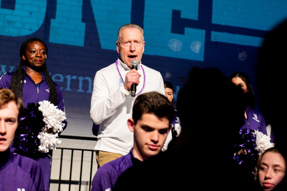 A person wearing white speaks into a microphone and addresses the crowd.