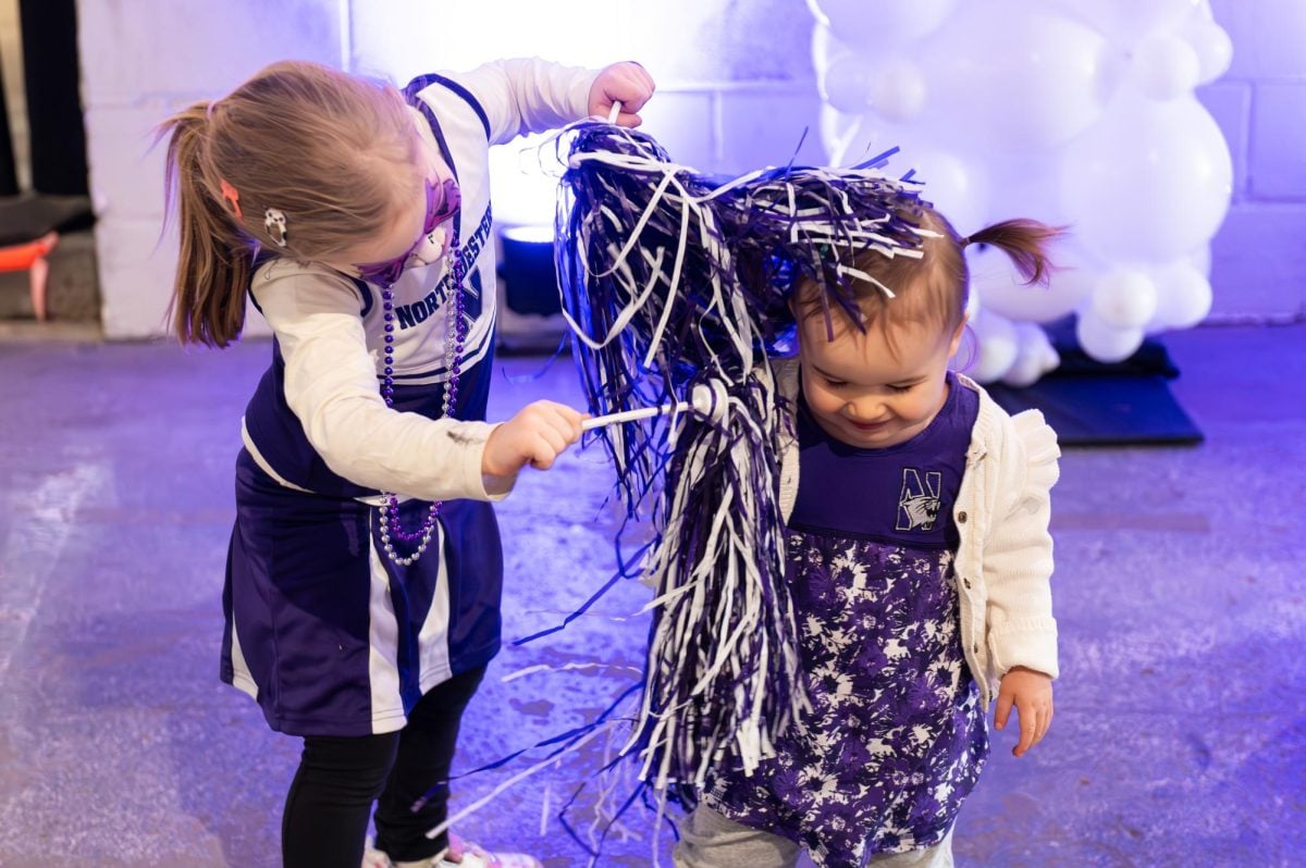 A child in purple waves pom poms to a younger child.