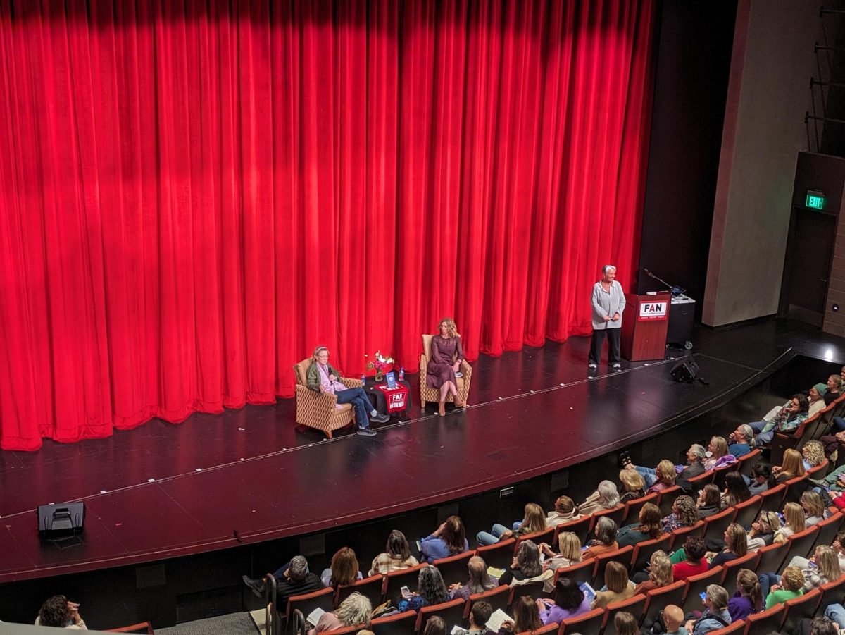 Three women on the stage and a large audience.