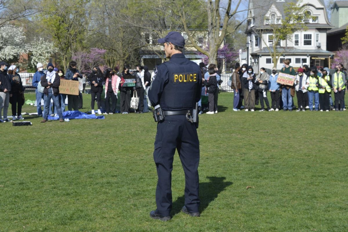 A+police+officer+stands+in+front+of+protesters+with+their+arms+linked+on+a+meadow.