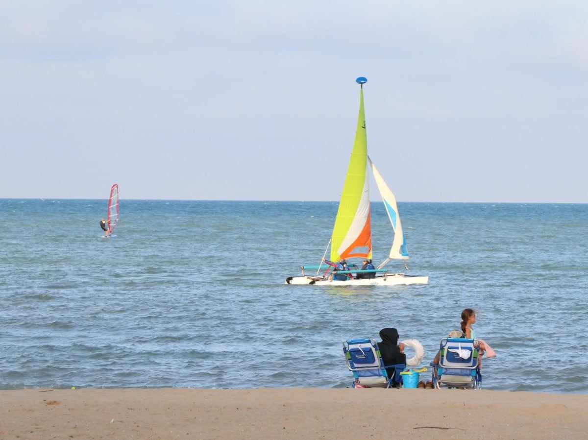 Two beach chairs are set up in the sand in front of a sailboat in the ocean.
