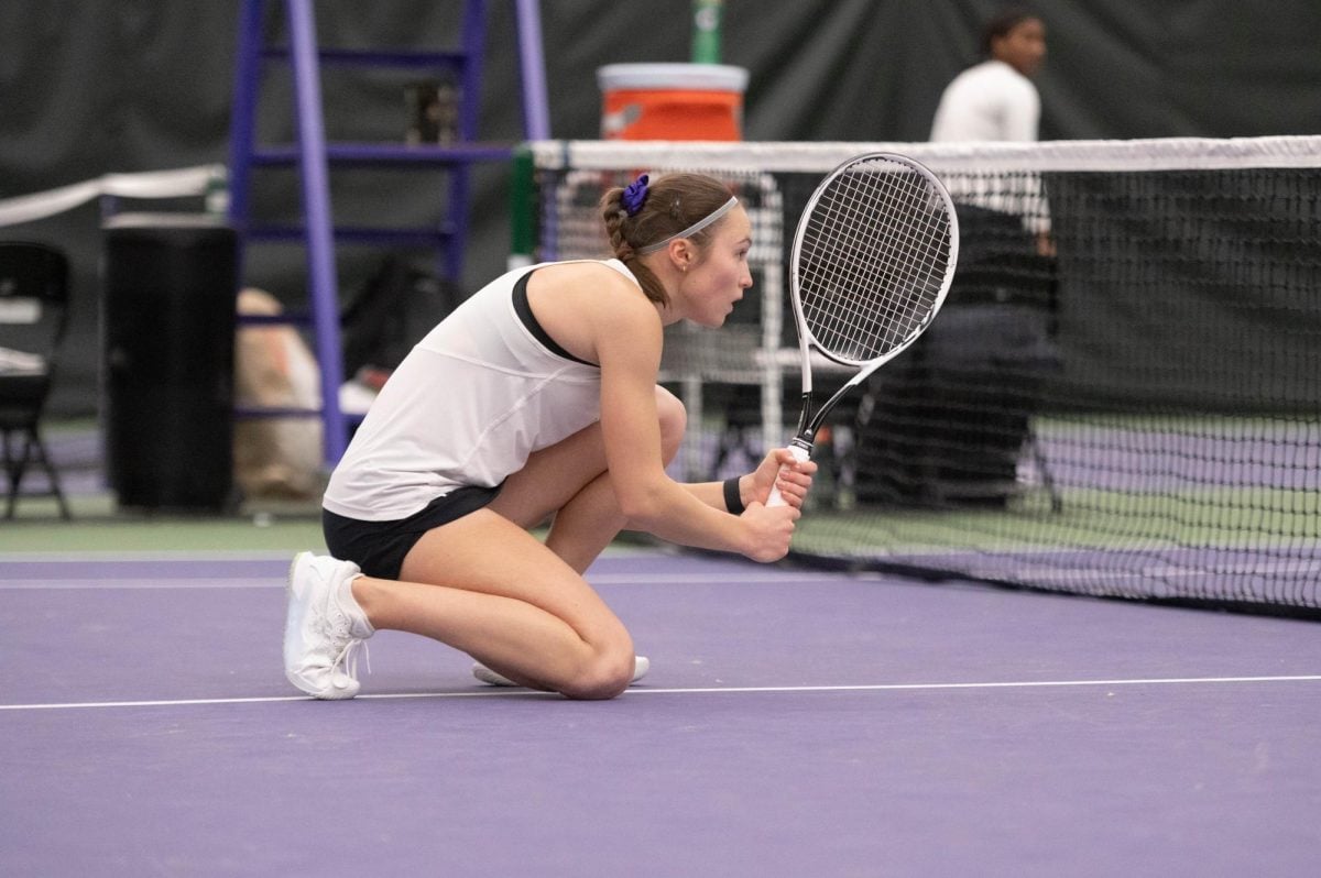 Northwestern senior Maria Shusharina kneels down on one knee while holding a tennis racket.