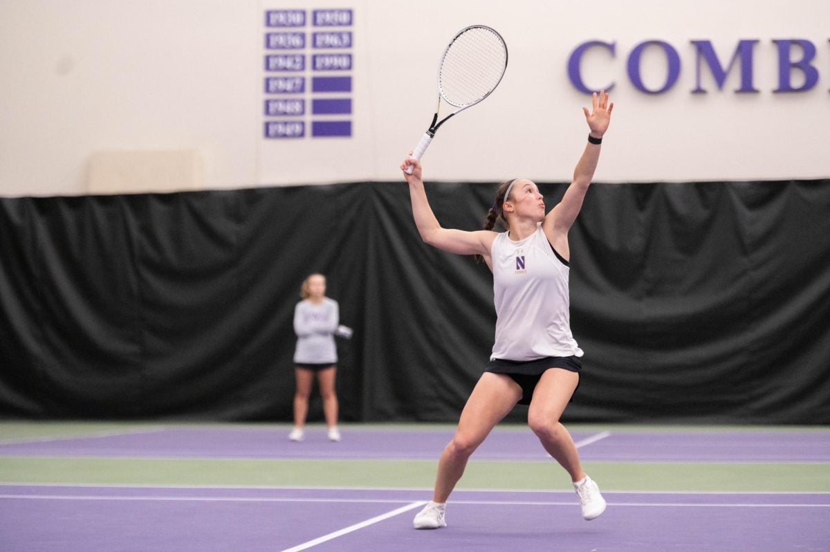 Looking upwards, Northwestern senior Maria Shusharina extends her arm with a tennis racket in hand, ready to serve the ball.