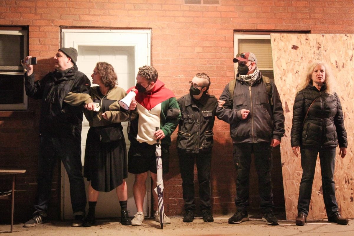 People stand under an outdoor apartment platform in front of a door.
