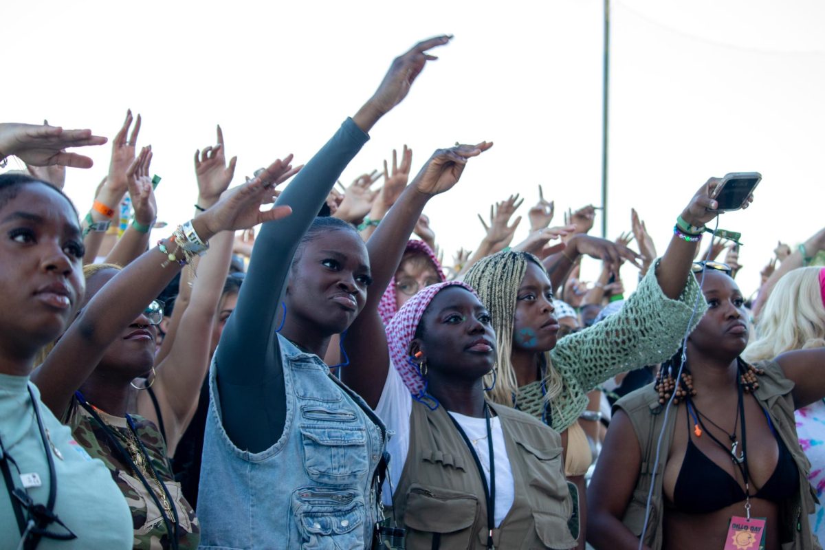 A group of people behind a concert barricade raise their arms toward the stage. 